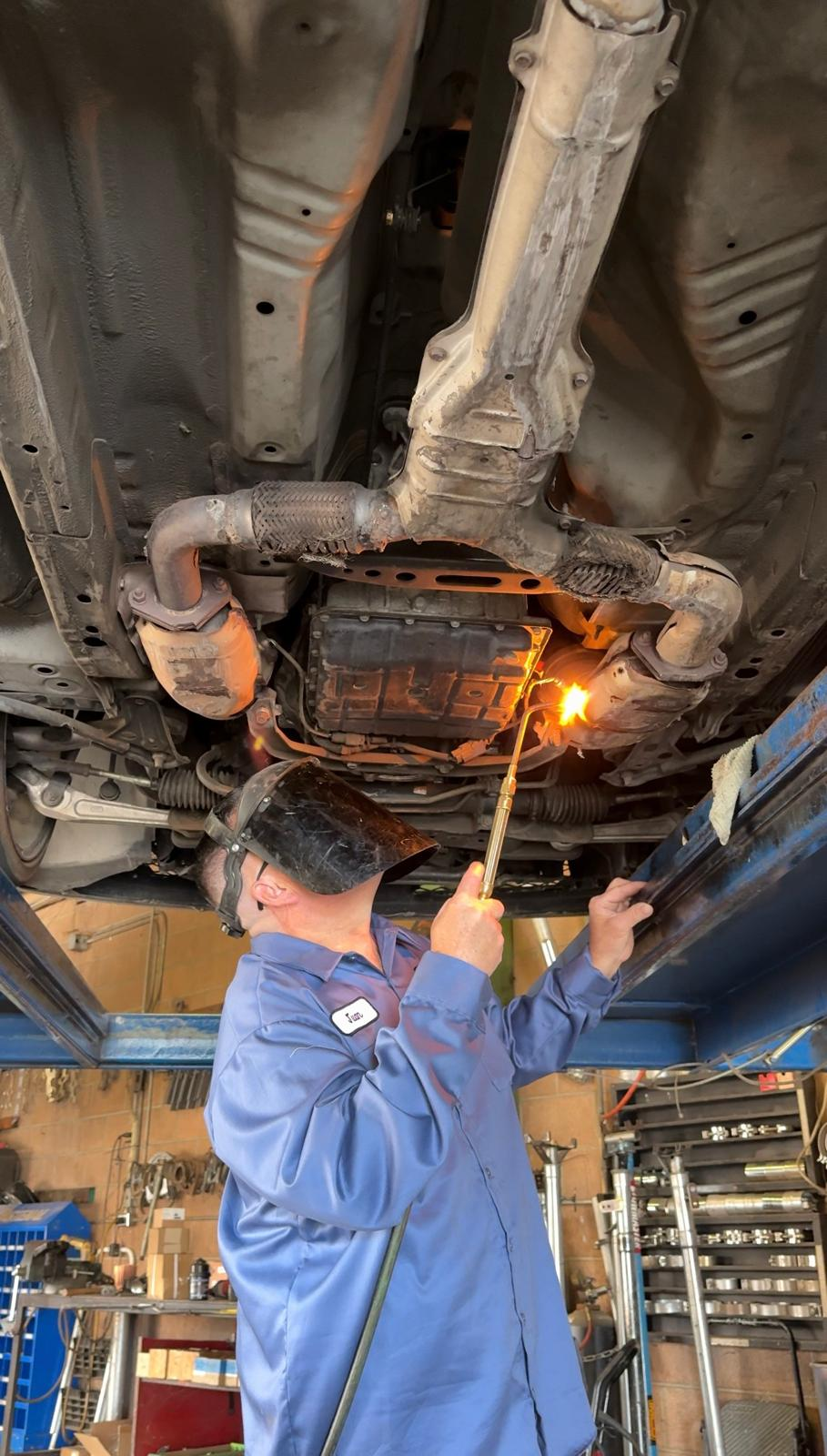 Mechanic working on exhaust under a vehicle